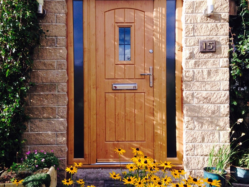 brown entrance door on brick house with yellow flowers at front