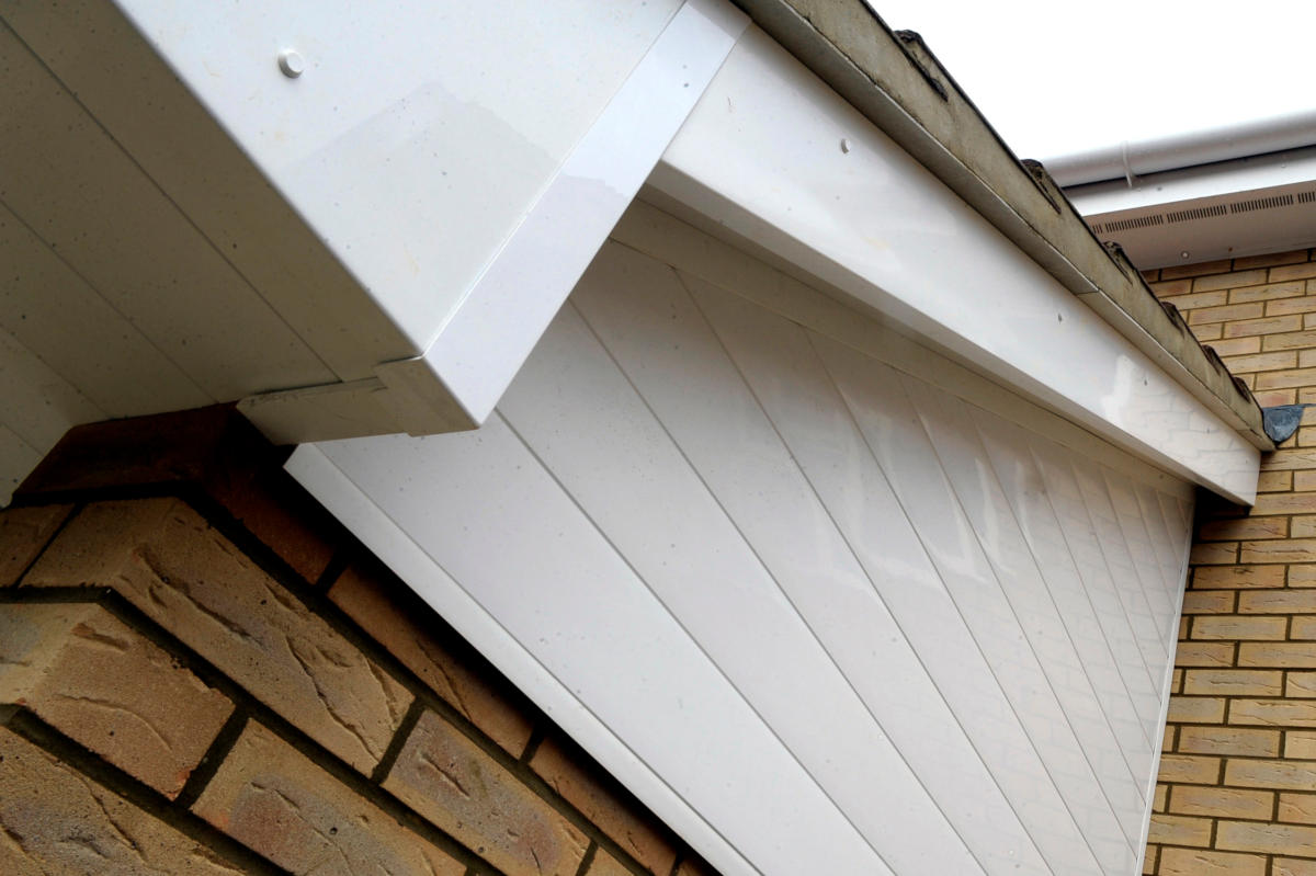 A close-up view of white UPVC cladding installed under the roofline of a brick house, showcasing the clean lines of the Feather Edge style with visible joints and fixings.