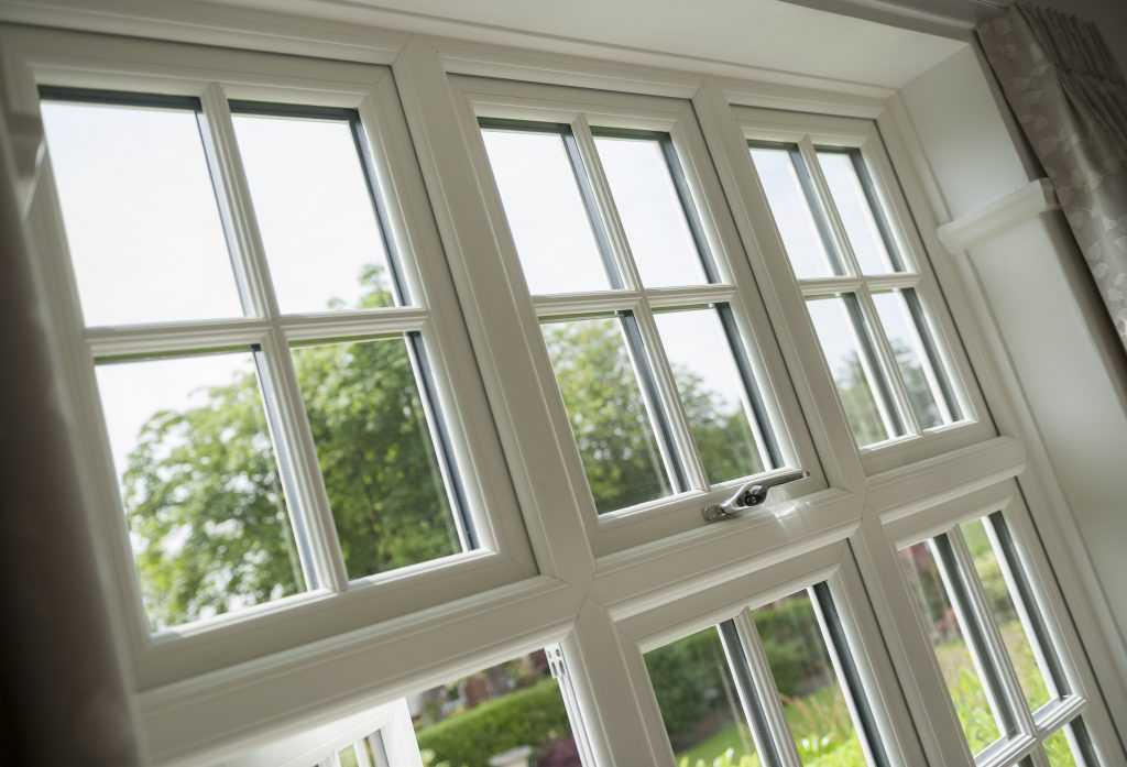 Interior view of a classic white framed window with Georgian bars, showcasing a view of lush greenery outside, complemented by soft, natural light.